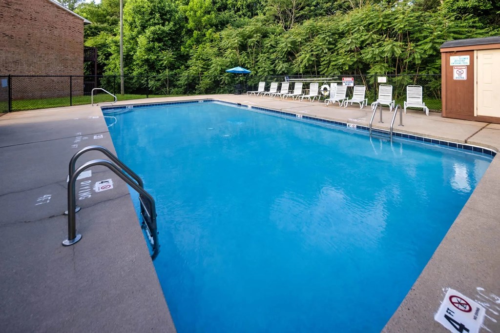 A pool with a blue tinted water and white chairs around it.