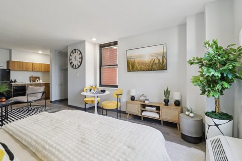 A modern bedroom with a large bed and a kitchen area in the background.