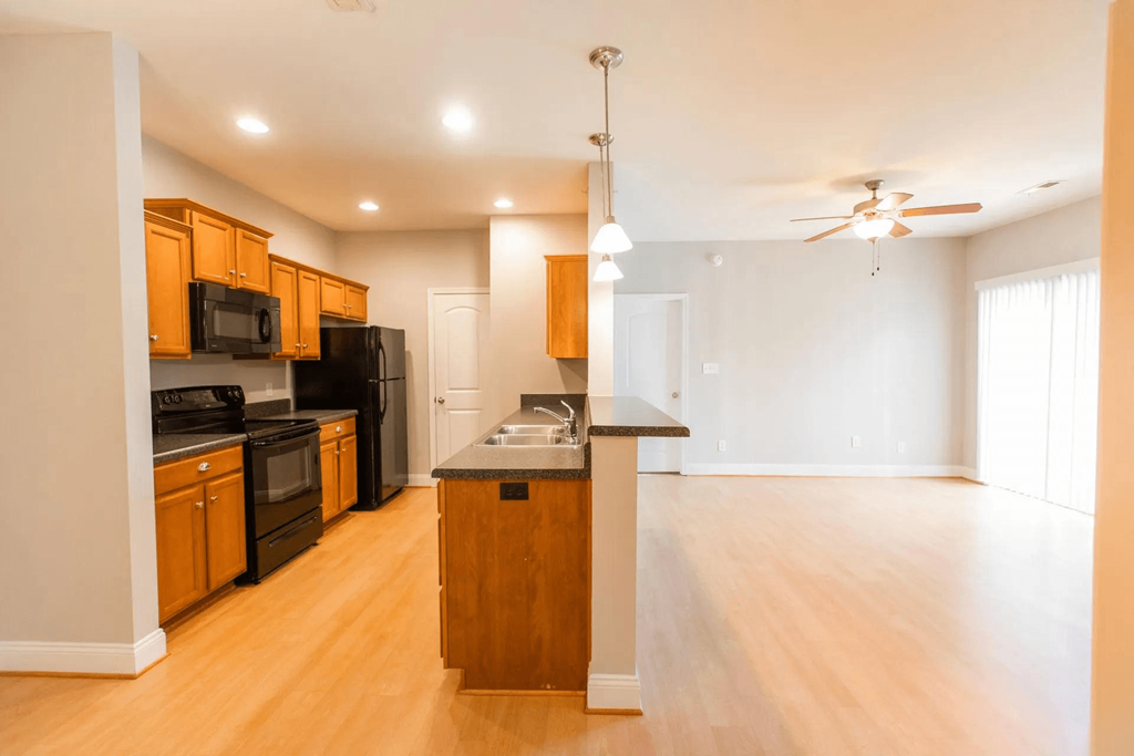 an empty kitchen and living room with wood floors and black appliances
