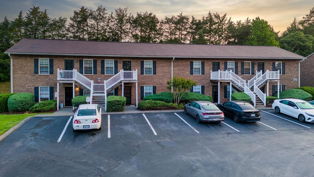 A parking lot in front of a brick building with cars parked.