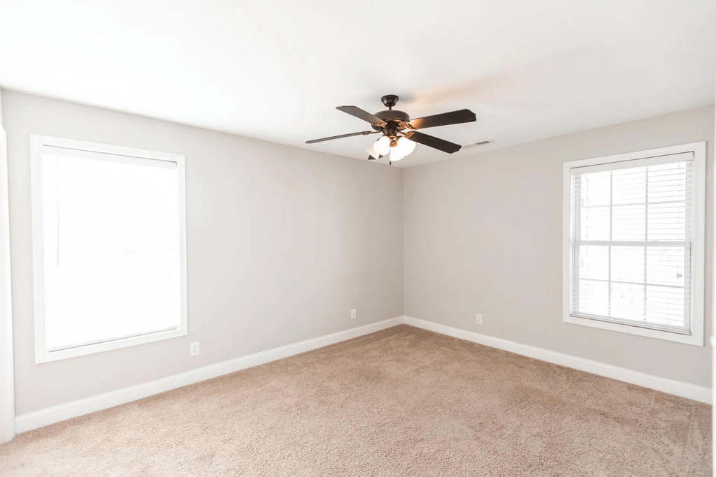 an empty bedroom with a ceiling fan and two windows