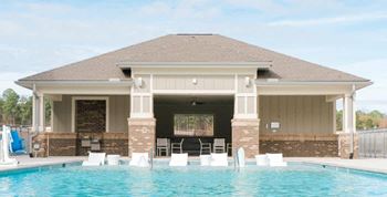 a swimming pool with chairs in front of a pool house