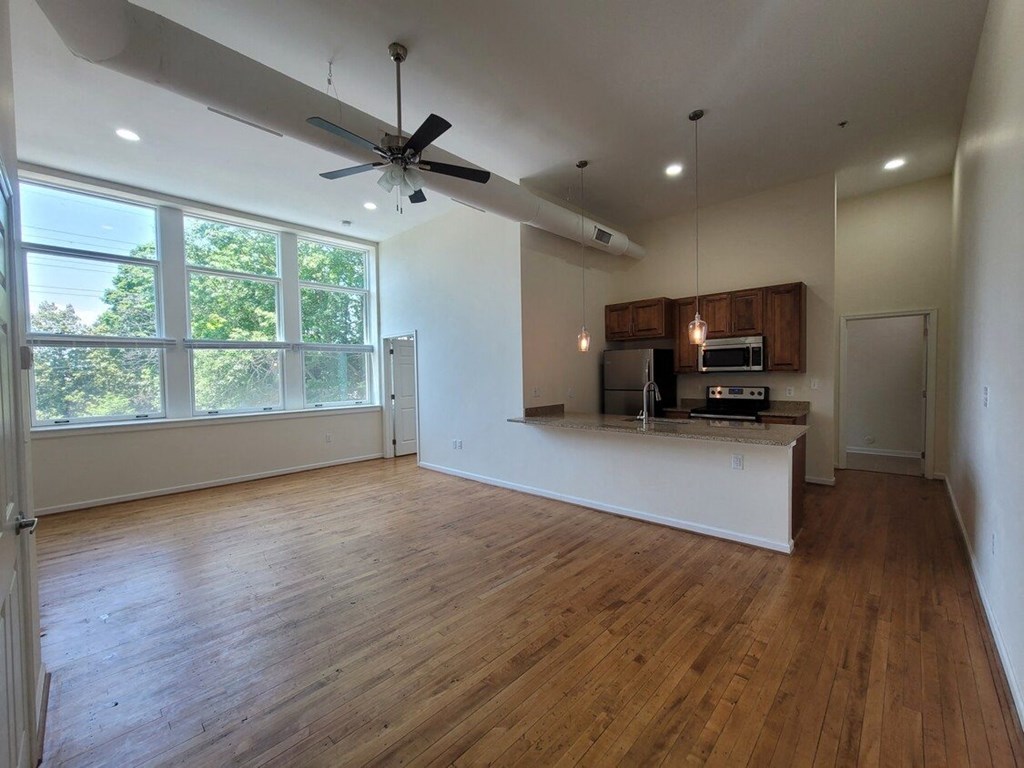 an empty living room with a kitchen and a ceiling fan