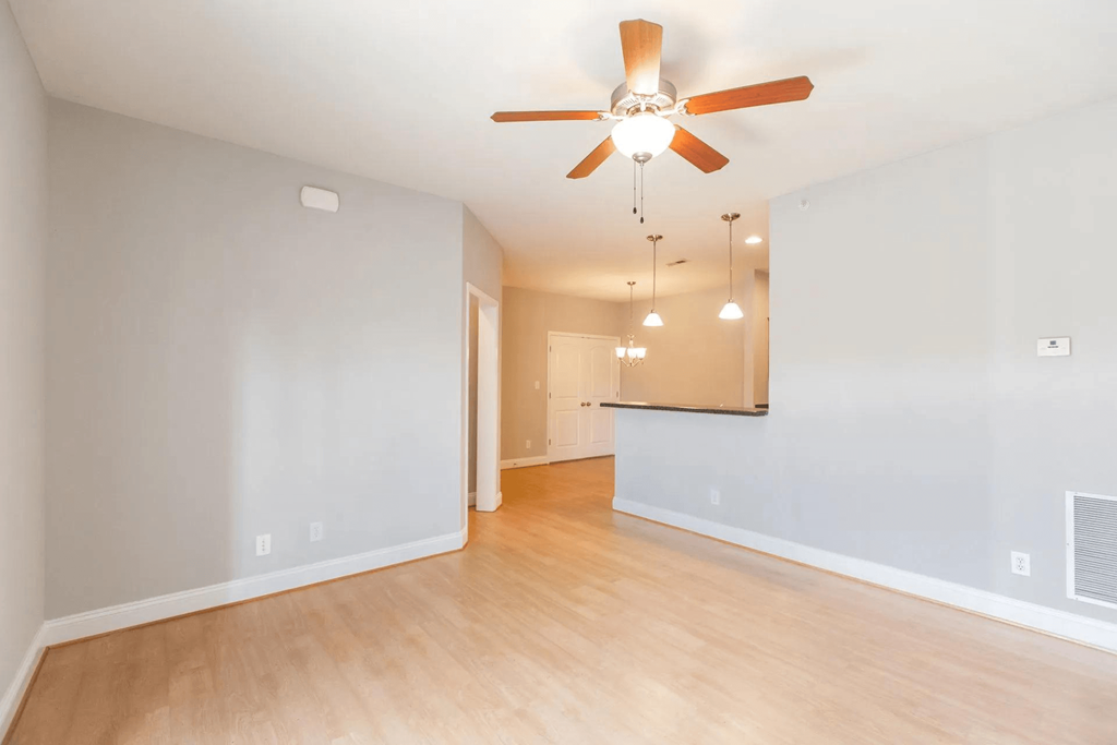 an empty living room with a ceiling fan and a kitchen