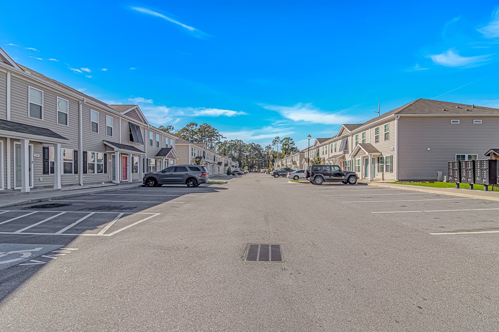 A parking lot in front of a row of townhouses with cars parked.
