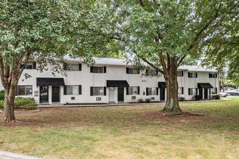 A white building with black awnings is surrounded by trees.