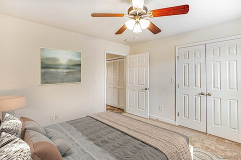 A bedroom with a bed, a ceiling fan, and a painting on the wall.