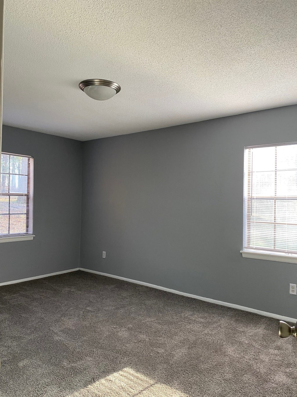 an empty room with gray walls and two windows