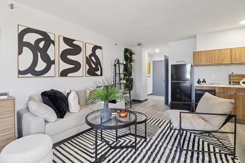 A living room with a black and white striped rug, a grey couch, a black chair, a glass coffee table, and three abstract paintings on the wall.