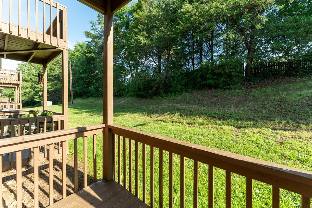 A wooden deck overlooks a grassy field and trees.