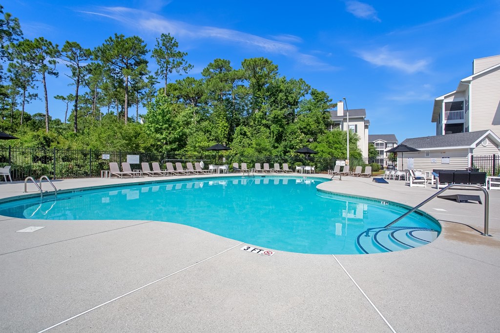 A large outdoor swimming pool surrounded by trees and apartment buildings.