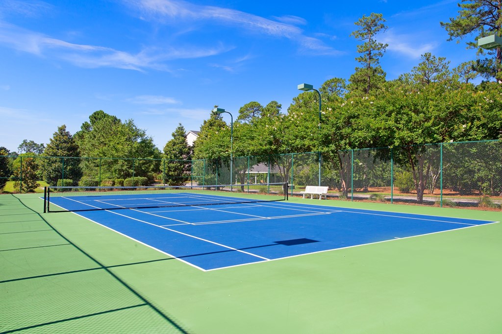 A tennis court surrounded by trees and a fence.