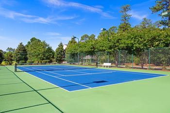 A tennis court surrounded by trees and a fence.