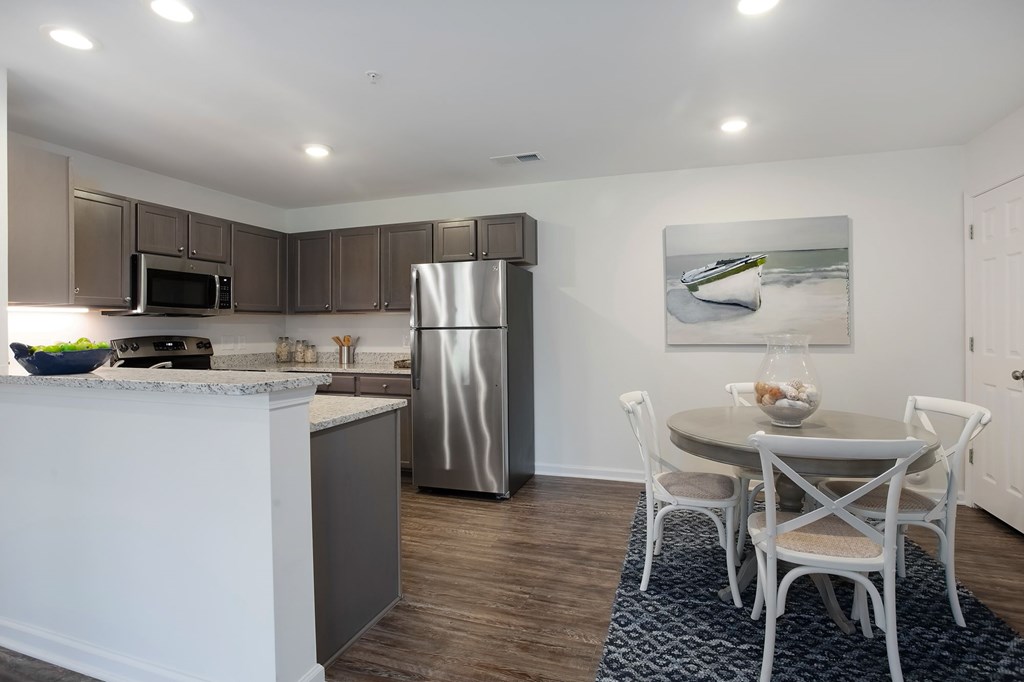 A kitchen with a refrigerator, microwave, and a dining table with chairs.