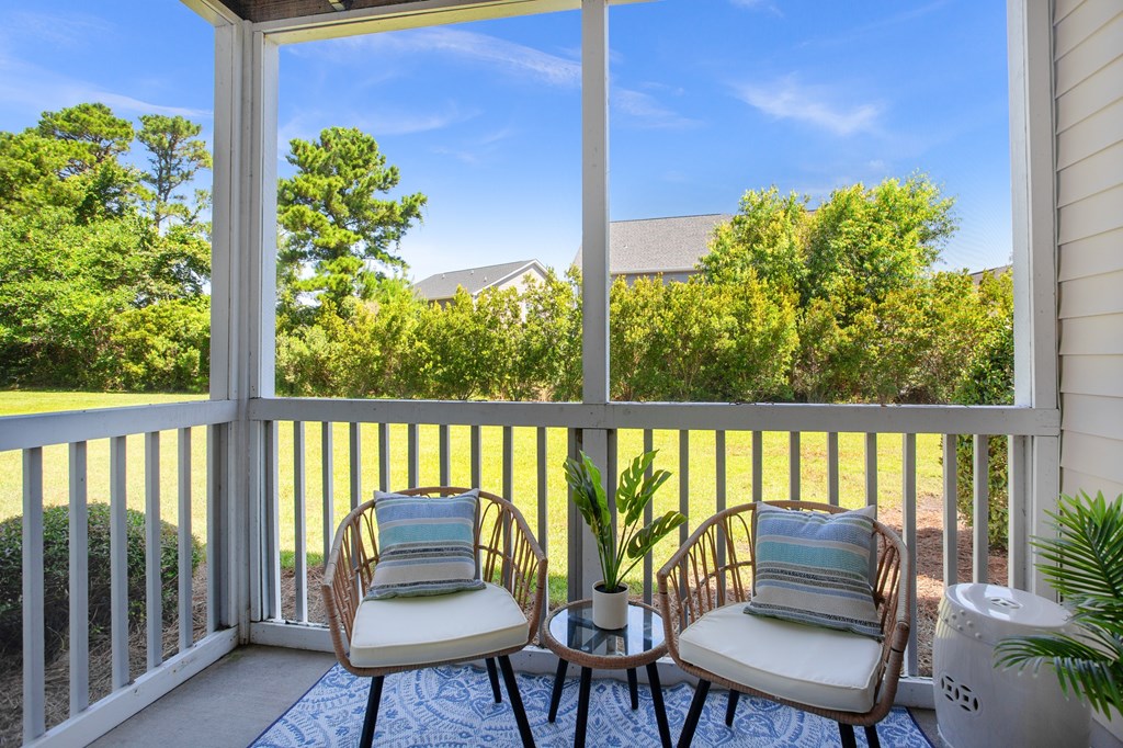 Two chairs are on a porch with a view of a house and trees.