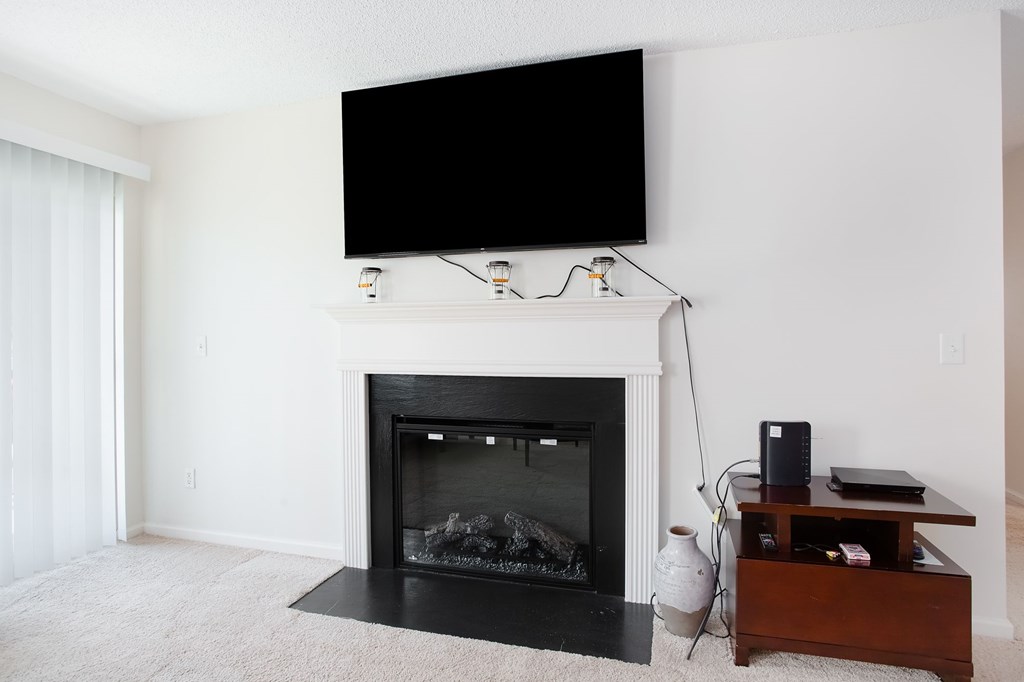 A black screen is mounted above a fireplace in a white room.