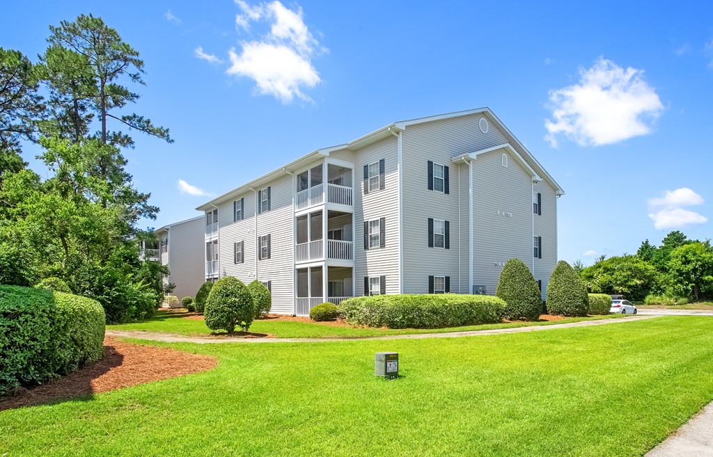 A large white apartment building with a green lawn in front.