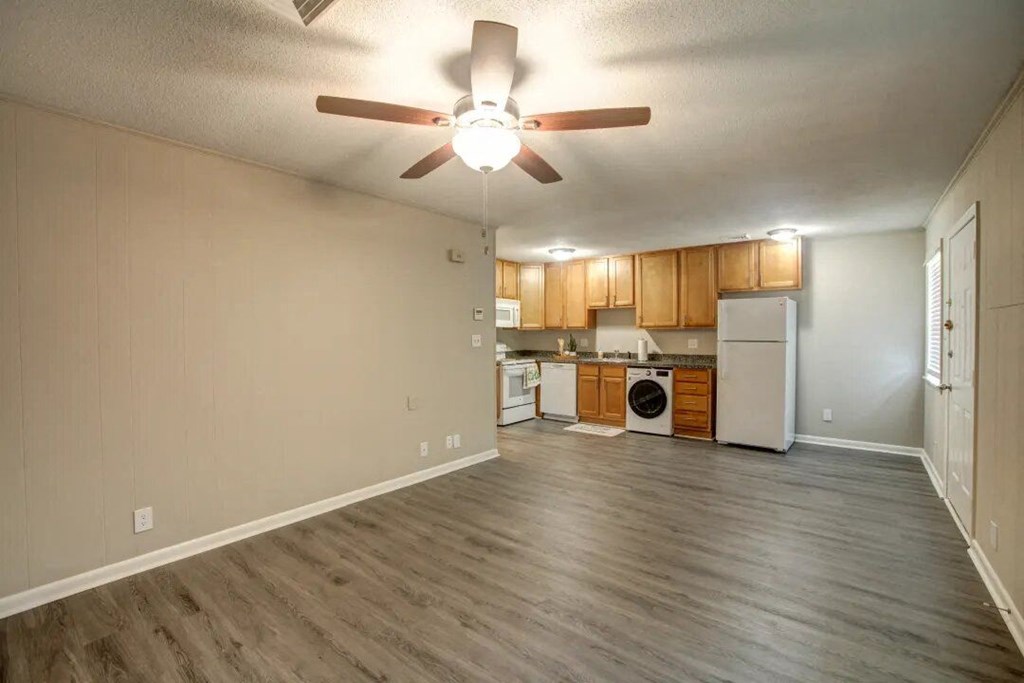 a living room with a ceiling fan and a kitchen in the background