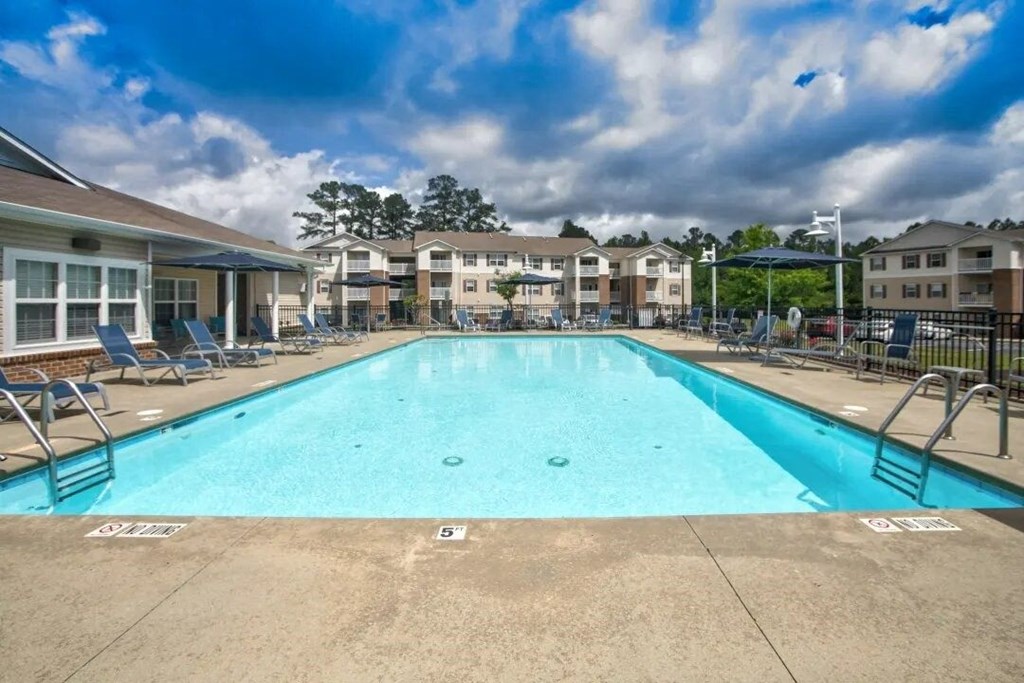 a swimming pool with chaise lounge chairs and apartment buildings in the background