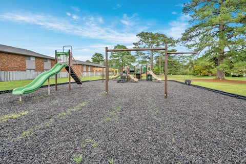 A playground with a green slide and a wooden swing set.