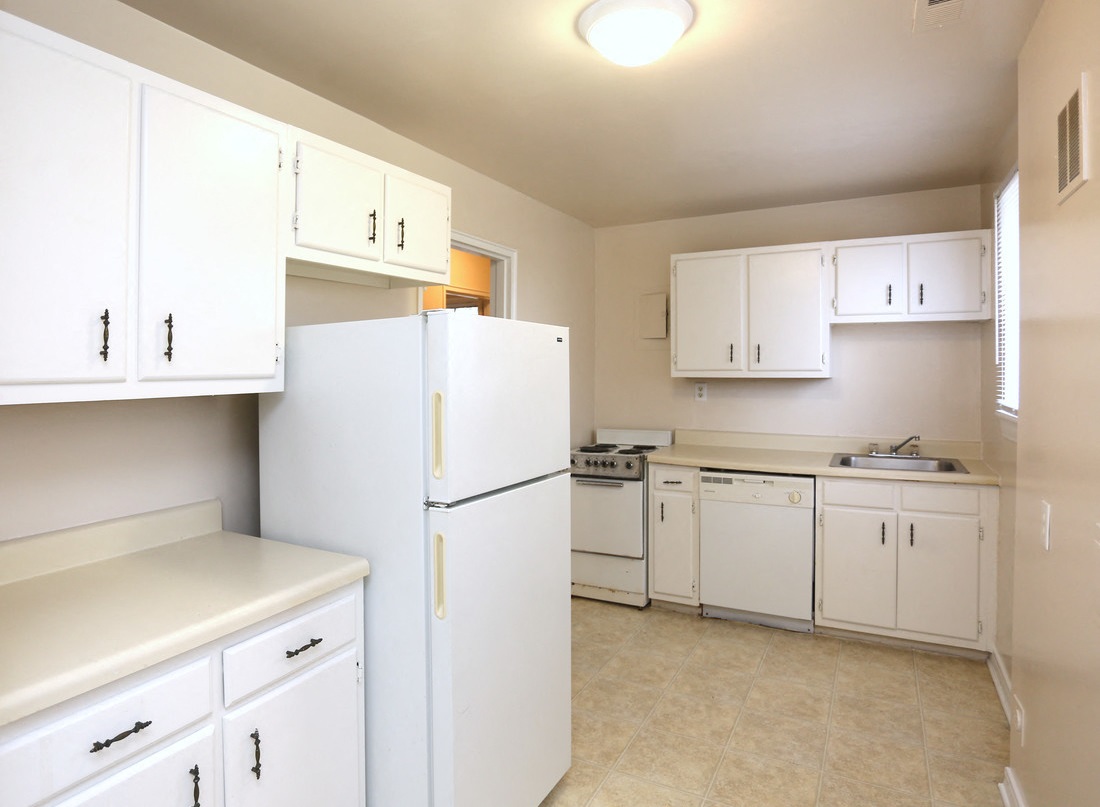 View of kitchen model with white cabinets, refrigerator, dishwasher, range