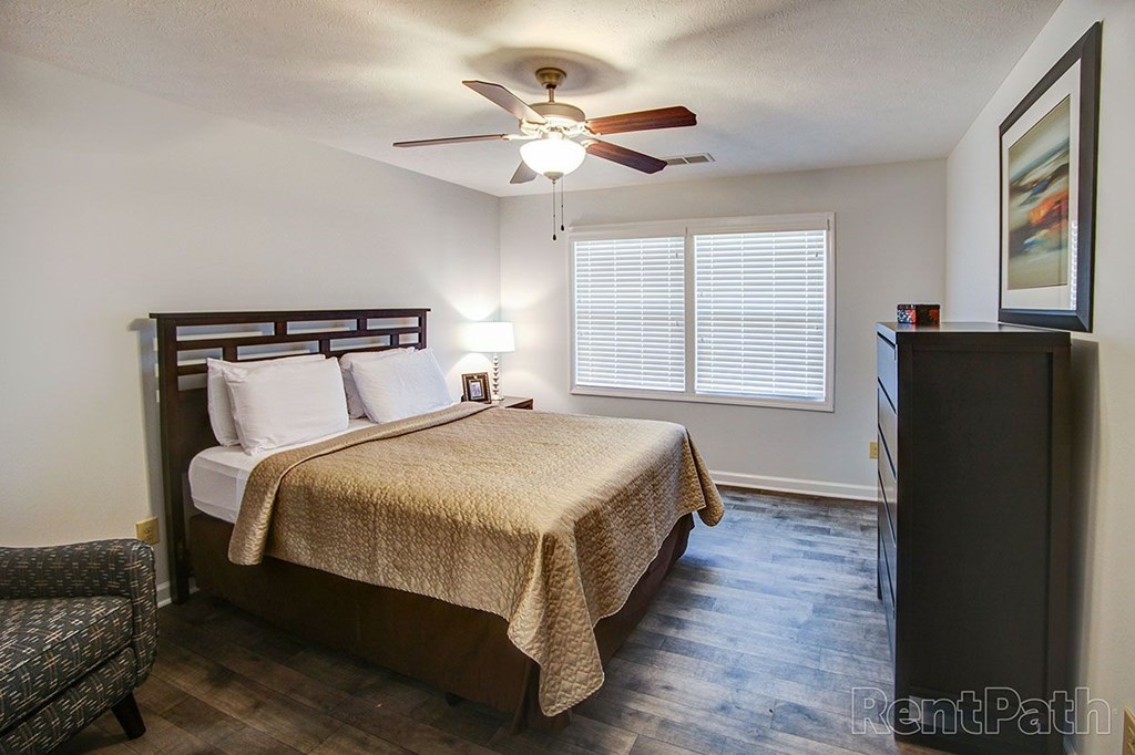 A bedroom with a bed, chair, and a ceiling fan.