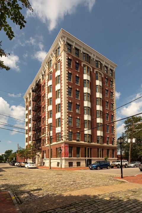 A tall red brick building with a flat roof and a parking lot in front.