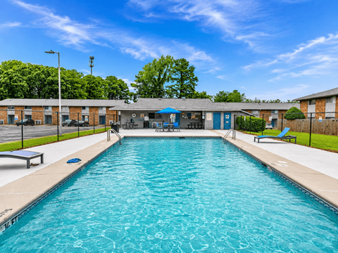 A large outdoor swimming pool with a blue sky and trees in the background.