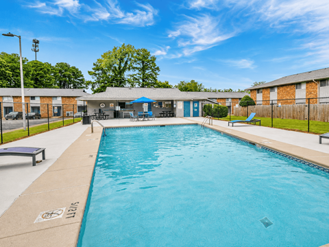 A large outdoor swimming pool with a blue sky and trees in the background.