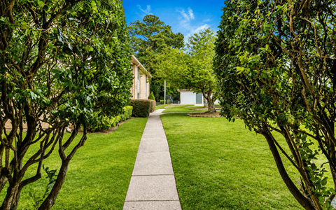 A pathway leads through a lush green garden to a white building.