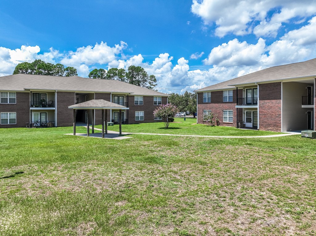 A grassy area in front of apartment buildings with a pavilion in the middle.