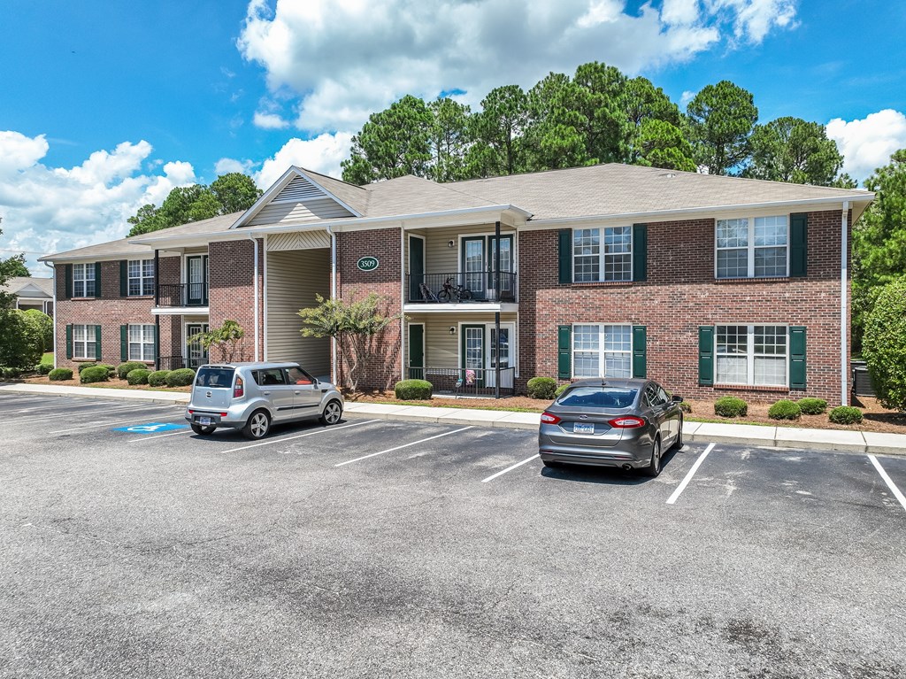 Two cars are parked in a parking lot in front of a brick apartment building.