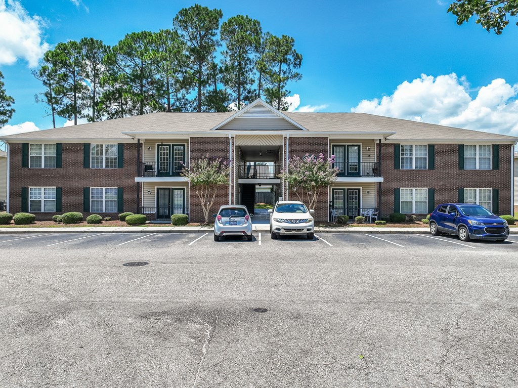 A parking lot in front of a brick building with two cars parked.