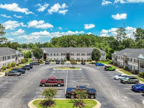 A parking lot with cars and a red truck in front of a building with trees in the background.