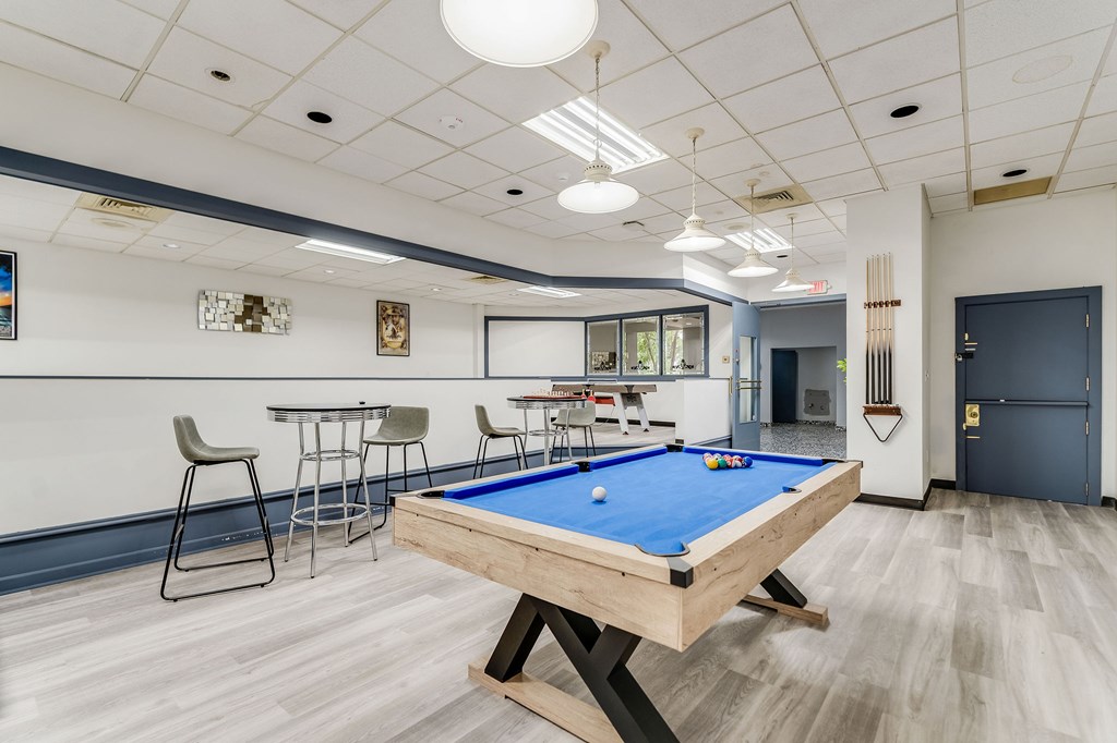 A pool table is in the middle of a room with a bar and chairs.