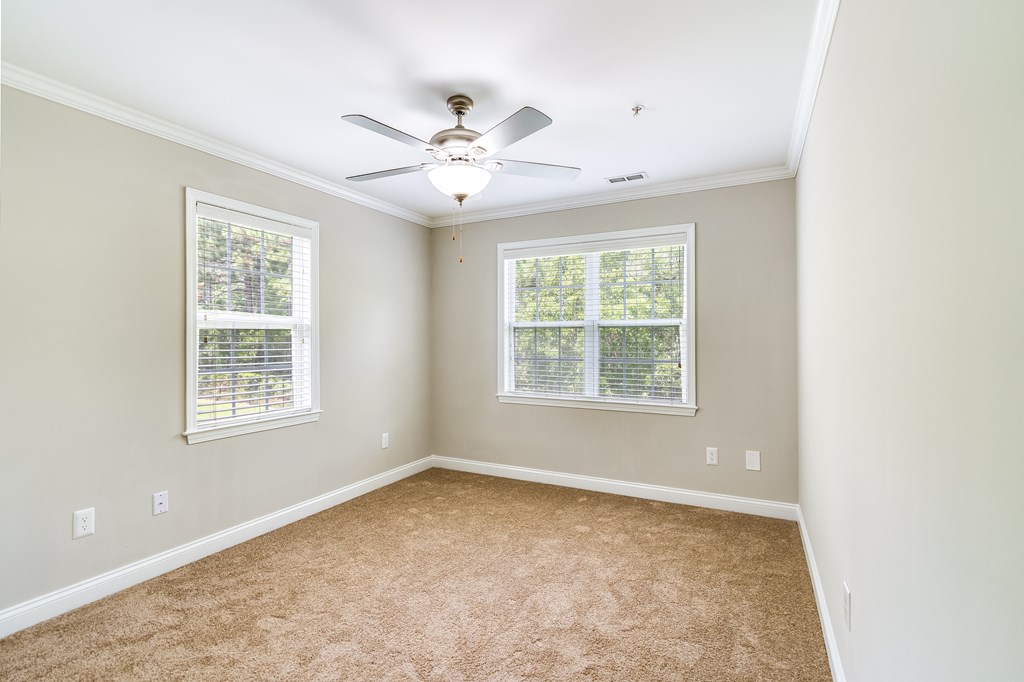 A room with a ceiling fan and two windows.