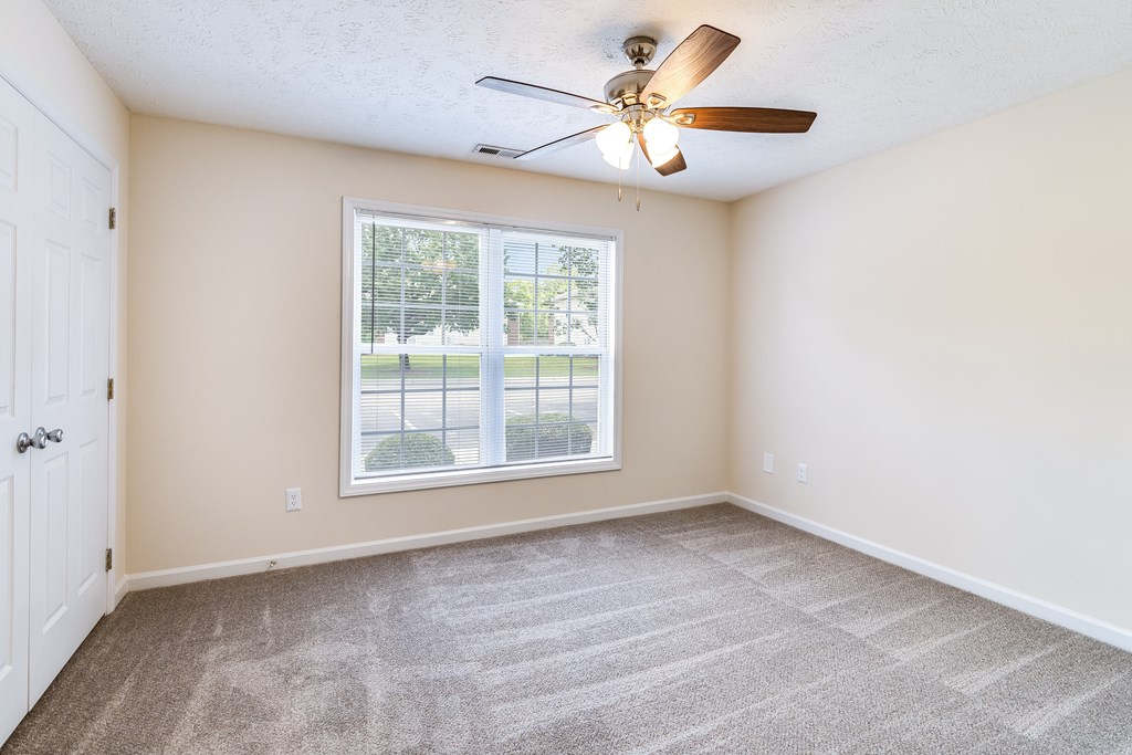 A room with a ceiling fan and a window overlooking a green area.