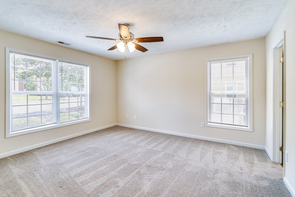 A room with a ceiling fan and two windows.
