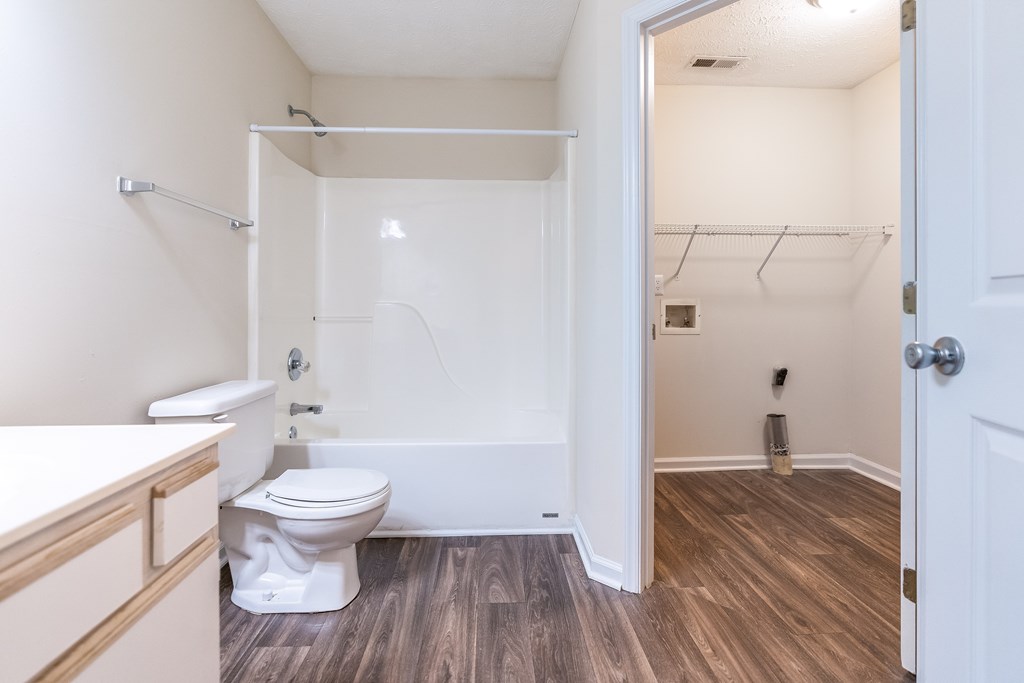 A white toilet sits in a small bathroom with wood flooring.
