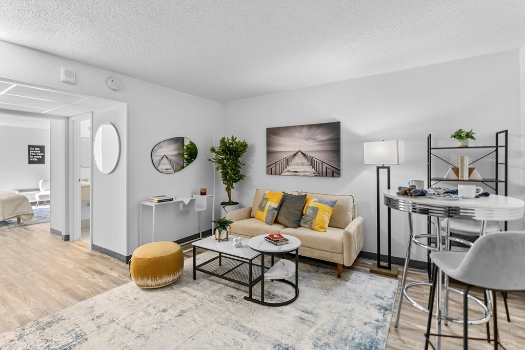 A living room with a yellow ottoman, a white couch, a coffee table, and a dining table with chairs.