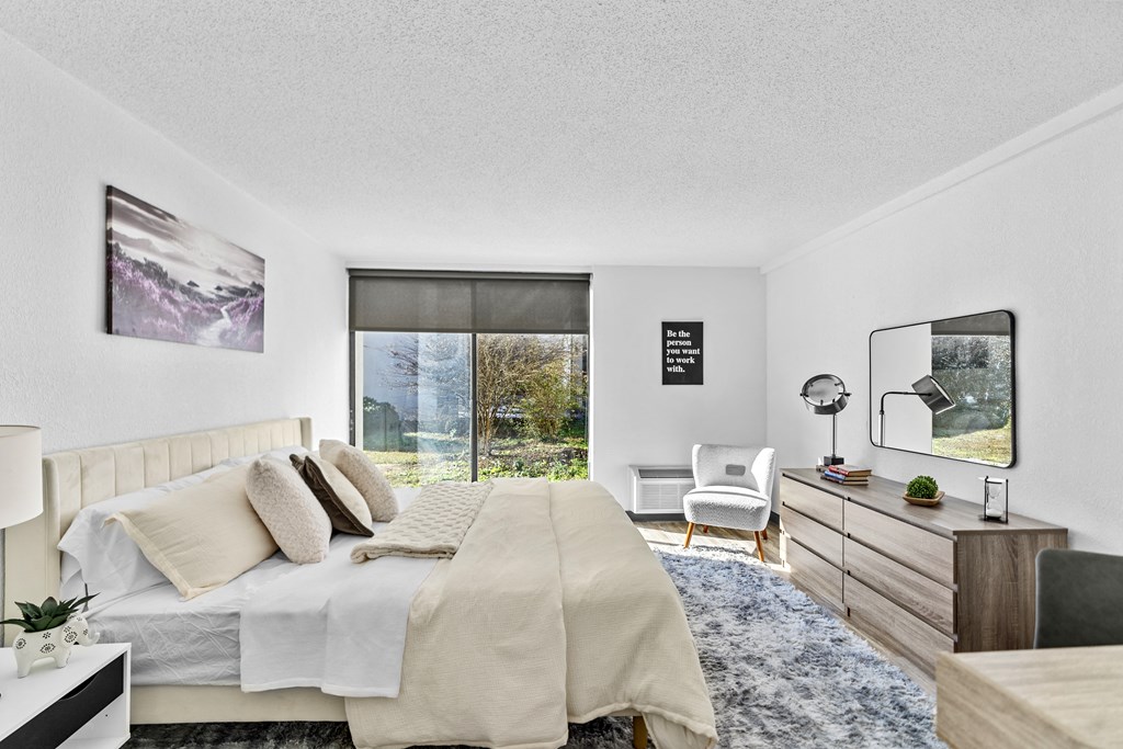 A bedroom with a large bed, a chair, and a window overlooking a garden.