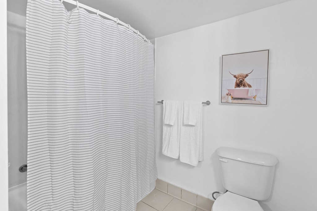 A bathroom with a toilet, a shower curtain, a towel, and a picture of a cow on the wall.