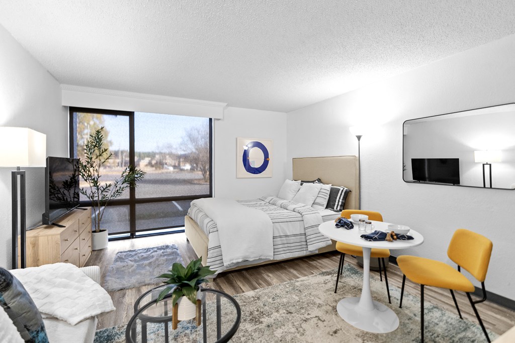 A bedroom with a bed, a chair, a table, and a mirror.