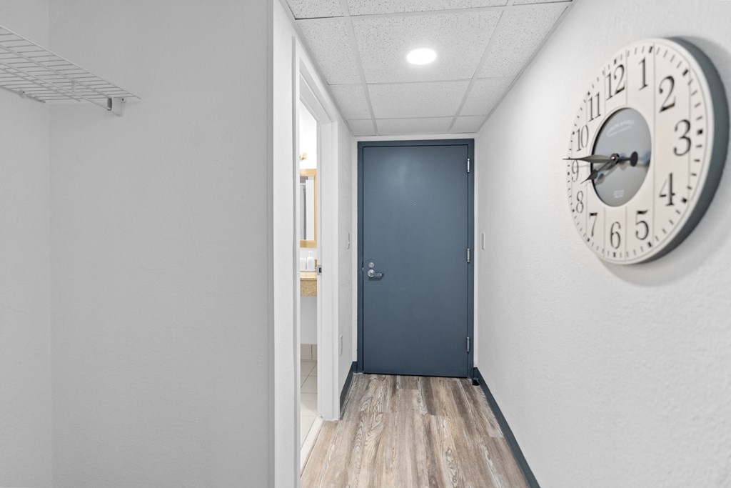 A hallway with a clock on the wall and a door at the end.