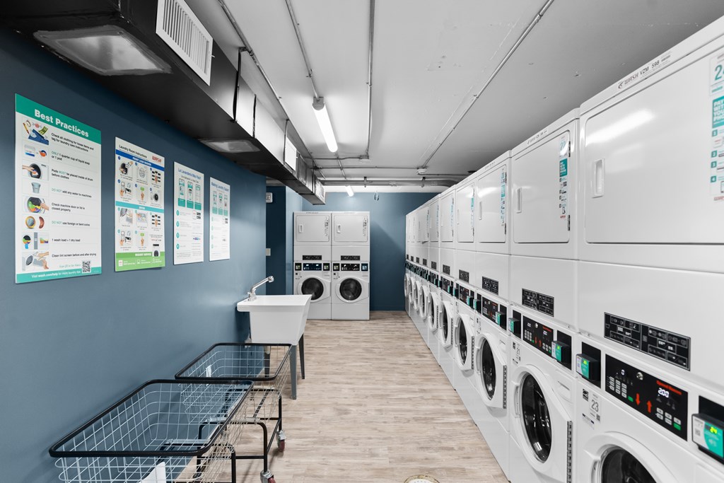 A laundromat with washers and dryers lined up and a sign on the wall.