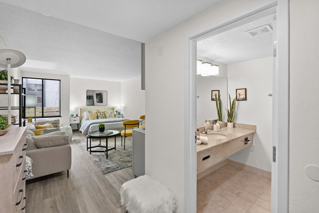 A white room with a bed, a couch, a table, and a plant.