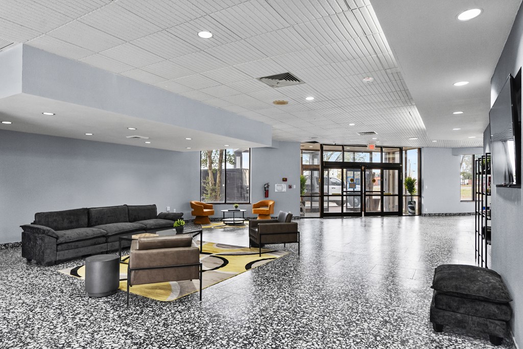 A grey couch and a yellow rug are in the middle of a white tiled floor.