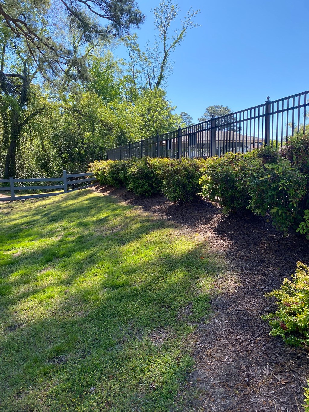A pathway in a garden with a white fence and green grass.