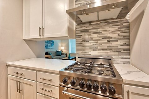 A modern kitchen with a stainless steel gas stove and white cabinets.