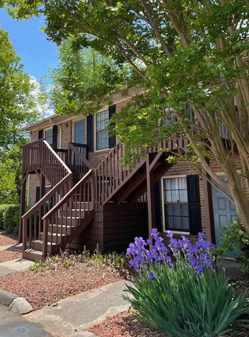 A house with a brown deck and a tree in front.